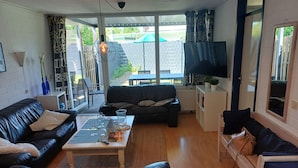 Een moderne woonkamer met een zwarte leren bank, een houten salontafel en een televisie op een standaard.