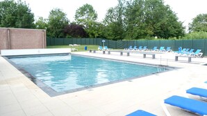 Une piscine rectangulaire, dotée d’une terrasse carrelée et entourée de chaises longues bleues.