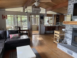 A cozy cabin interior with a fireplace, wooden floors, a dining area, and a kitchen. - Cottage on Moon River w/ Fantastic Deck! (pet friendly) (MacTier)