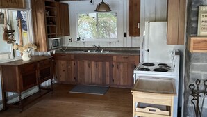 Maalaishenkinen keittiö, jossa on puukaapit, keskellä oleva keittiösaareke, liesi ja pesuallas.