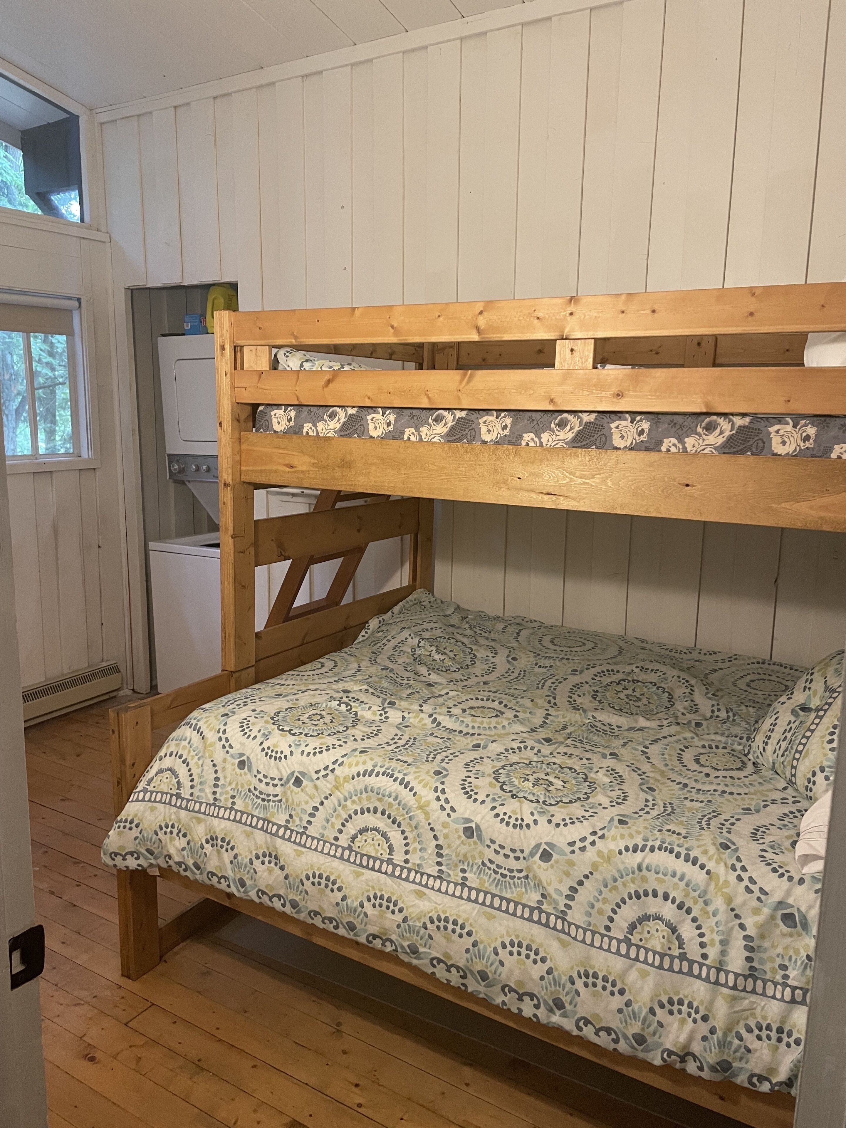 A bunk bed with a patterned bedspread in a room with wooden walls and a window.