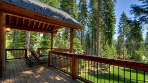 A wooden deck with a pergola, a lounge chair, and a view of a forested area. - Lazy Bear Lodge in Homewood - hot tub, close to lake, large home (Homewood)