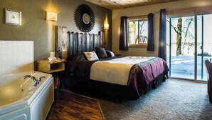 Ein Schlafzimmer mit einem Bett, einem Holz-Kopfteil, einem Wandspiegel, einem kleinen Nachttisch mit Lampe und einem Fenster mit Vorhängen.