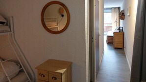 A narrow hallway with a bunk bed on the left, a wooden dresser, and a round mirror on the wall. A door leads to a room with a bed and a dresser. - 50m from resort center, 3rd floor, balcony, parking, tv, ski locker, 32m², Les 2 Alpes (Les Deux Alpes)