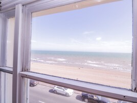 Vista de una playa a través de una ventana, con una carretera y coches en primer plano.