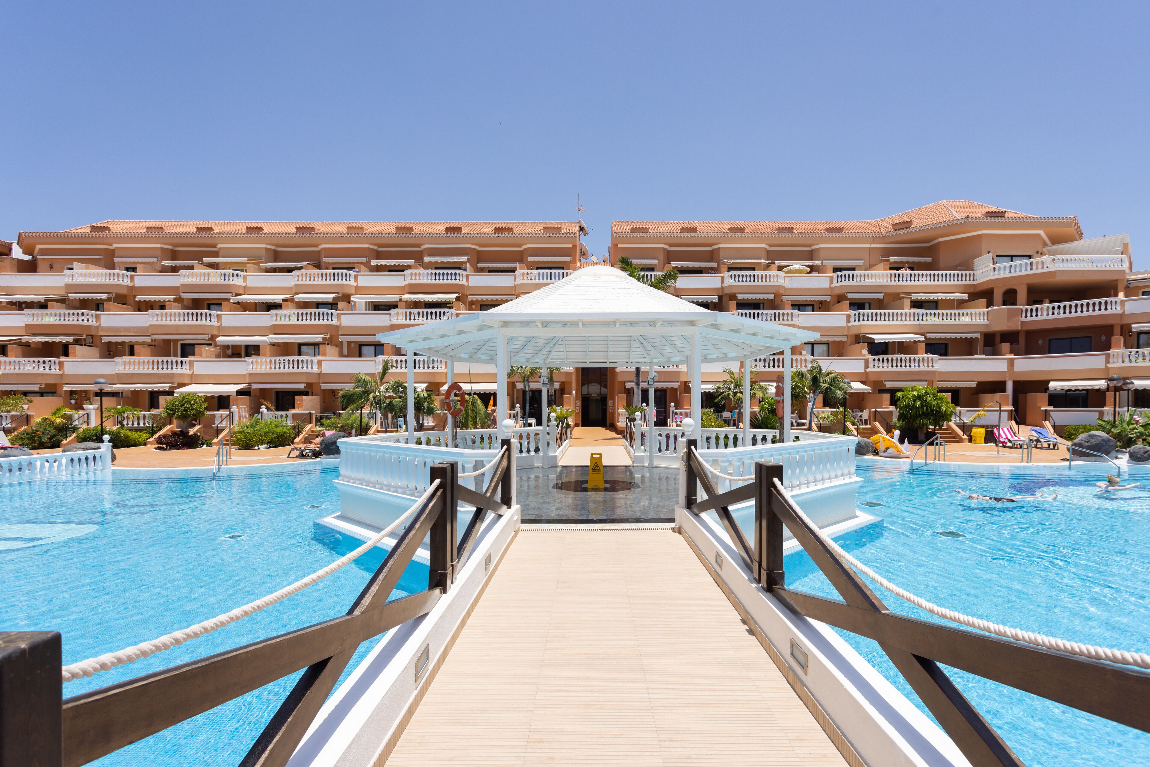 Un hotel con piscina central, pasillo cubierto y varios balcones.