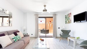 Uma sala de estar moderna com um sofá, uma mesa de centro de vidro, uma poltrona e uma TV fixada na parede.