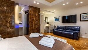 Een hotelkamer met een groot bed, een donker leren bank, een flatscreen televisie en een schilderij aan de muur.