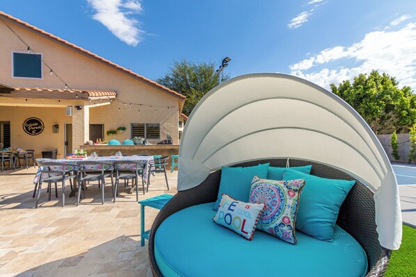 A cozy outdoor seating area with a white curved canopy, a wicker sofa with teal cushions, and a table set for dining.