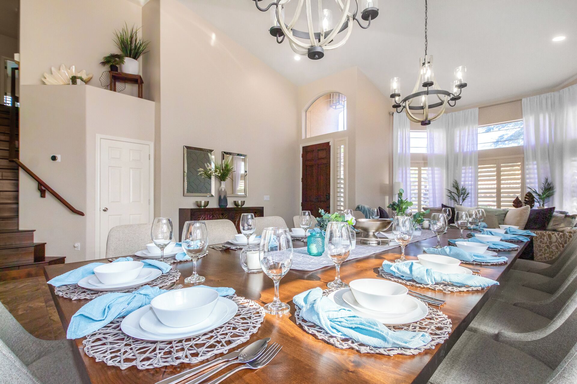 A dining room with a long table set for a meal, a chandelier, and a staircase.