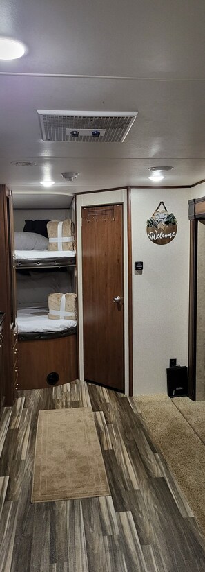 A compact room with a bunk bed, a wooden door, a welcome sign, and a small rug on the floor. - Family Friendly Lake View Front at Coconuts Beach RV Resorts (Gravois Mills)
