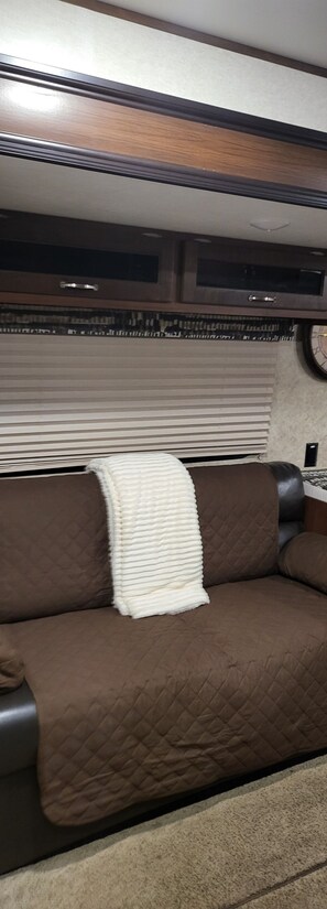 A brown couch with a white throw blanket, a window with blinds, and a wall-mounted clock. - Family Friendly Lake View Front at Coconuts Beach RV Resorts (Gravois Mills)