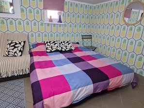 A bedroom with a bed, pillows, a bedside table, a mirror, and a window with a curtain.