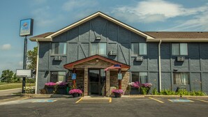 A two-story motel with a stone facade, a central entrance with an American flag, and a parking lot with handicapped parking spaces. - Star of The Lakes (Detroit Lakes)