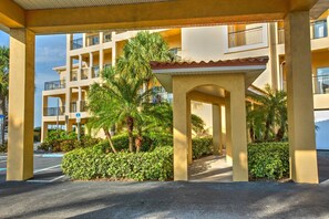 A covered outdoor area with a palm tree and a building with balconies in the background. - Private Waterfront Balcony! Steps From the Beach, Heated Pool, with Nearby Grocery & Restaurants. (Treasure Island)