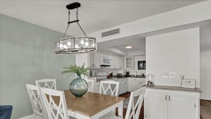 A modern kitchen with white cabinetry, a wooden dining table, and a hanging light fixture. - Station One 6F - a beautifully updated 2 bedroom condo (Wrightsville Beach)