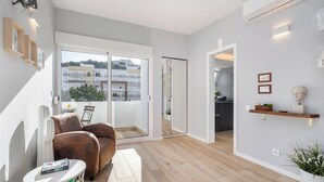 Een moderne woonkamer met een bruine leren bank, een klein rond tafeltje met een tijdschrift, en een groot raam met uitzicht op gebouwen en groen.