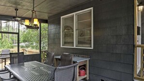 Un patio techado al aire libre con una mesa y sillas, una lámpara colgante y una ventana con persianas.