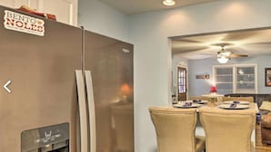 Una cocina compacta con refrigerador, un comedor con mesa y sillas, y una sala de estar con sofá y lámpara.