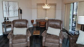 Een woonkamer met twee bruine leren fauteuils, een houten salontafel, een kroonluchter en een schilderij aan de muur.