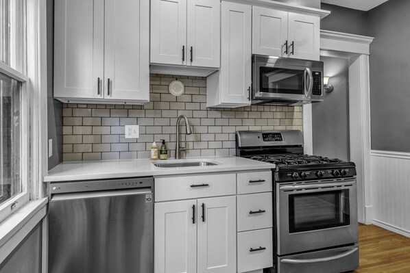 Une cuisine moderne avec des meubles blancs, un lave-vaisselle en acier inoxydable, un four à micro-ondes encastré et une cuisinière à gaz.