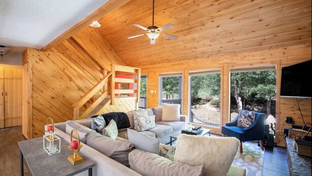 Ein Holzblockhaus-Interieur mit einer Couch, einem blauen Sessel, einem Tisch mit Kerze und einem Deckenventilator.
