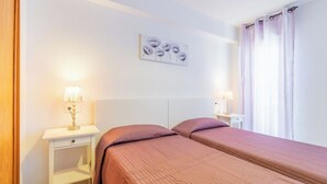 Une chambre d’hôtel avec deux lits, une tête de lit blanche, une table de chevet avec une lampe et un tableau au mur.