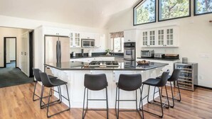 Una cocina moderna con una isla central, taburetes de bar y ventanas amplias.