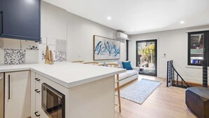 A modern kitchen with white cabinetry, a central island, and a dining area with a sofa and rug.