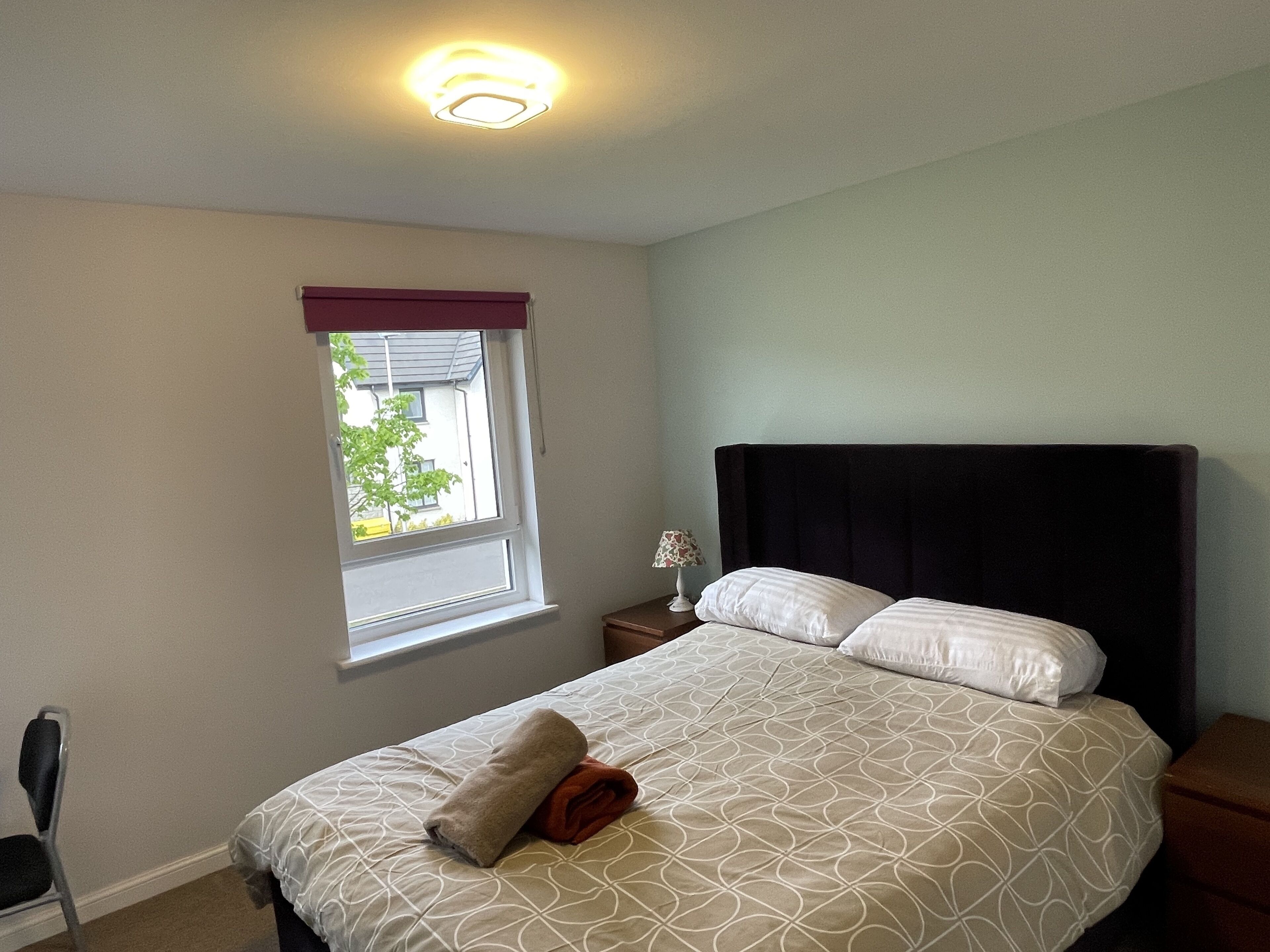 A bedroom with a bed, a window with a view, a nightstand, and a lamp.