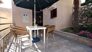 An outdoor patio with a table and chairs, a green umbrella, and a stone wall with plants. - 100 metres to the pebble beach (Baska)