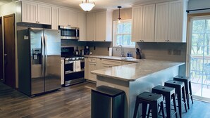 A modern kitchen with white cabinets, stainless steel appliances, and a large island with bar stools. - Relaxing 3 Bedroom Home in Lake Community (Albrightsville)