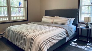 A bedroom with a bed, two windows, a nightstand, and an American flag. - Relaxing 3 Bedroom Home in Lake Community (Albrightsville)