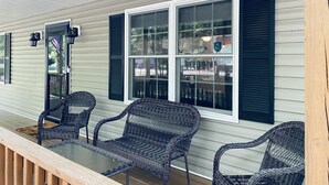 A covered porch with three wicker chairs and a glass table, white siding, and black shutters. - Relaxing 3 Bedroom Home in Lake Community (Albrightsville)