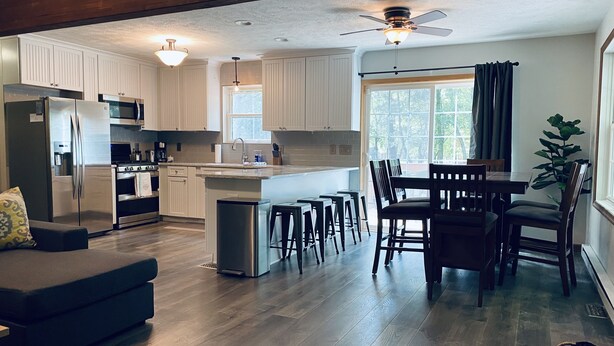 A modern kitchen with white cabinets, stainless steel appliances, and a central island with bar stools. - Relaxing 3 Bedroom Home in Lake Community (Albrightsville)