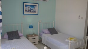Un dormitorio con dos camas individuales, una mesita de noche con lámpara y un cuadro en la pared.