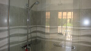 Ducha con puerta de cristal, baranda y vista a un balcón con mobiliario exterior.
