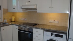 Cocina con armarios blancos, horno empotrado, lavadora y encimera de granito.