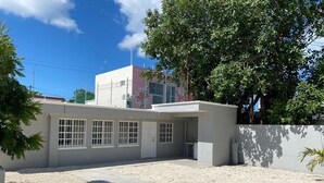 Un edificio moderno con techo plano, ventanas grandes y un sendero de hormigón que lleva a una entrada con portón.