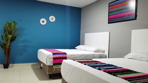 Una habitación con dos camas, una pared azulada, una planta y una obra de arte colorida.