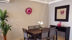 Un comedor con una mesa redonda, seis sillas, una planta en maceta y un espejo colgado en la pared.