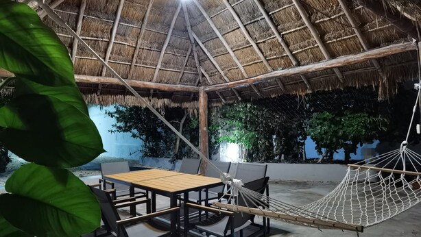 Un espacio al aire libre con techo de paja, una hamaca, una mesa y sillas.