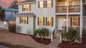 Une maison à deux étages avec un porche à l’avant, un balcon à l’étage supérieur et un petit jardin devant la maison, agrémenté d’aménagements paysagers.