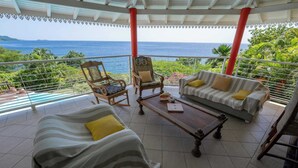 A balcony with a view of the sea, furnished with a sofa, chairs, and a table.