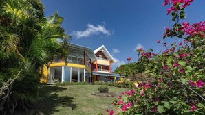 A two-story house with a balcony, surrounded by lush greenery and vibrant flowers.