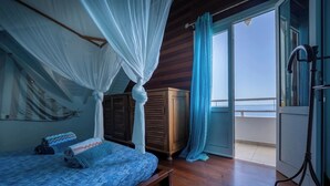 A bedroom with a bed, a wooden wardrobe, a balcony with a view, and a curtain.