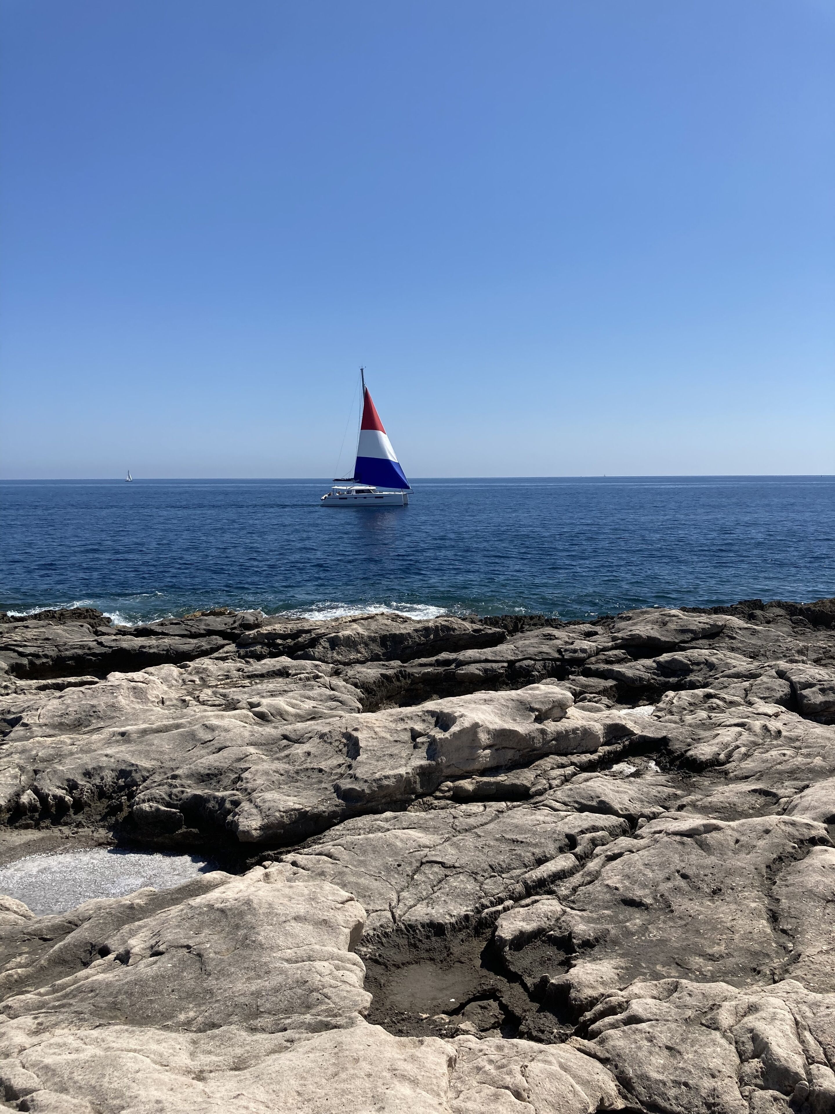 A sailboat with a red, white, and blue sail on a calm sea.