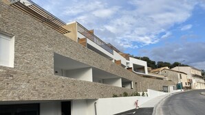 A modern building with a stone facade, multiple balconies, and a curved driveway.