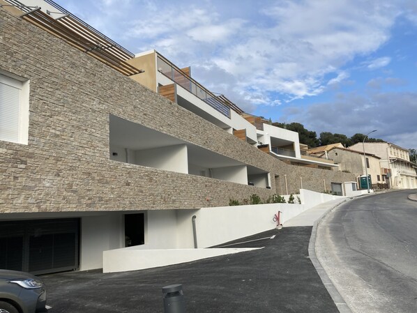 A modern building with a stone facade, multiple balconies, and a curved driveway.
