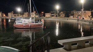 A marina at night with boats docked, a bench, and buildings in the background.